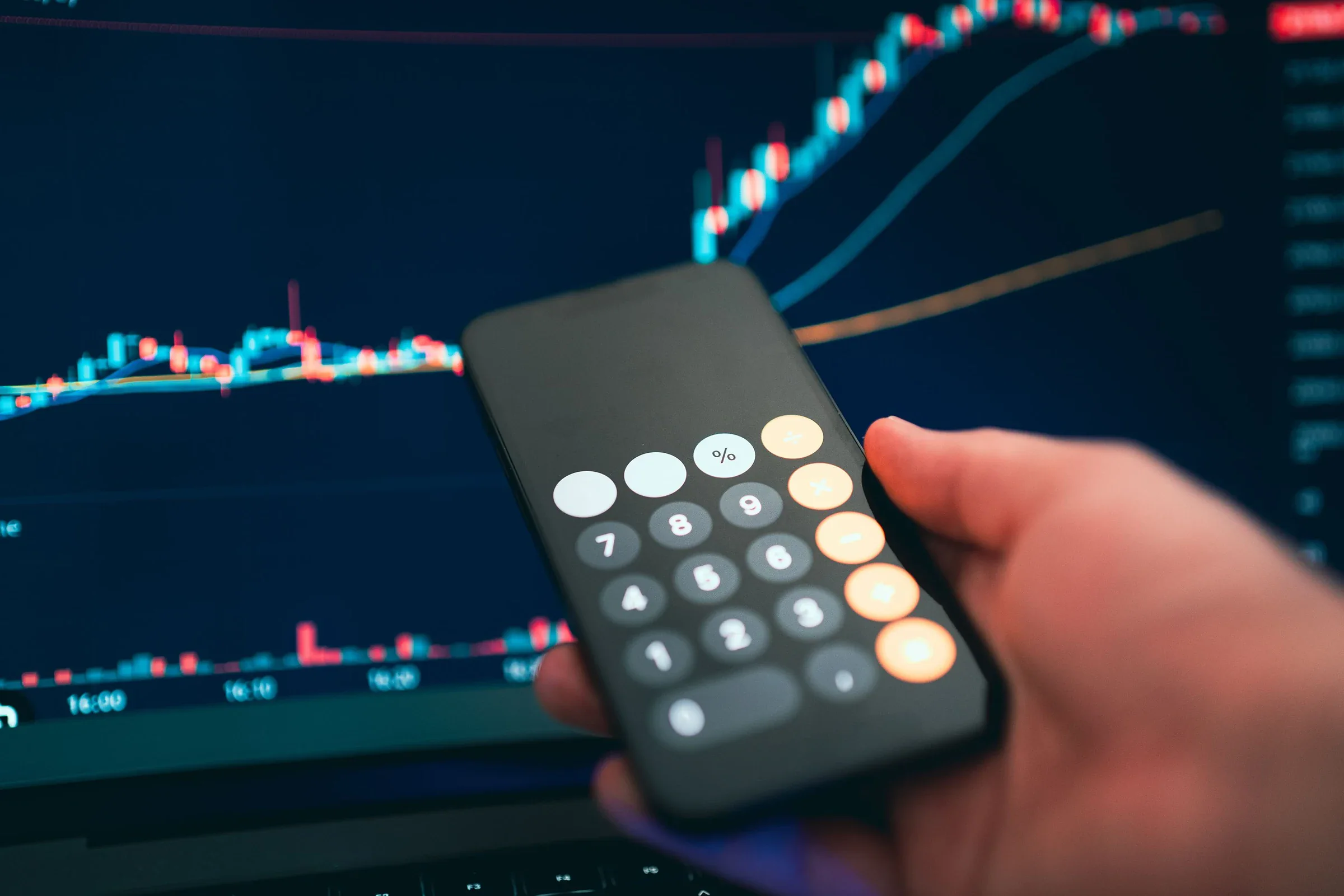 Calculator held over a market chart while reviewing position size